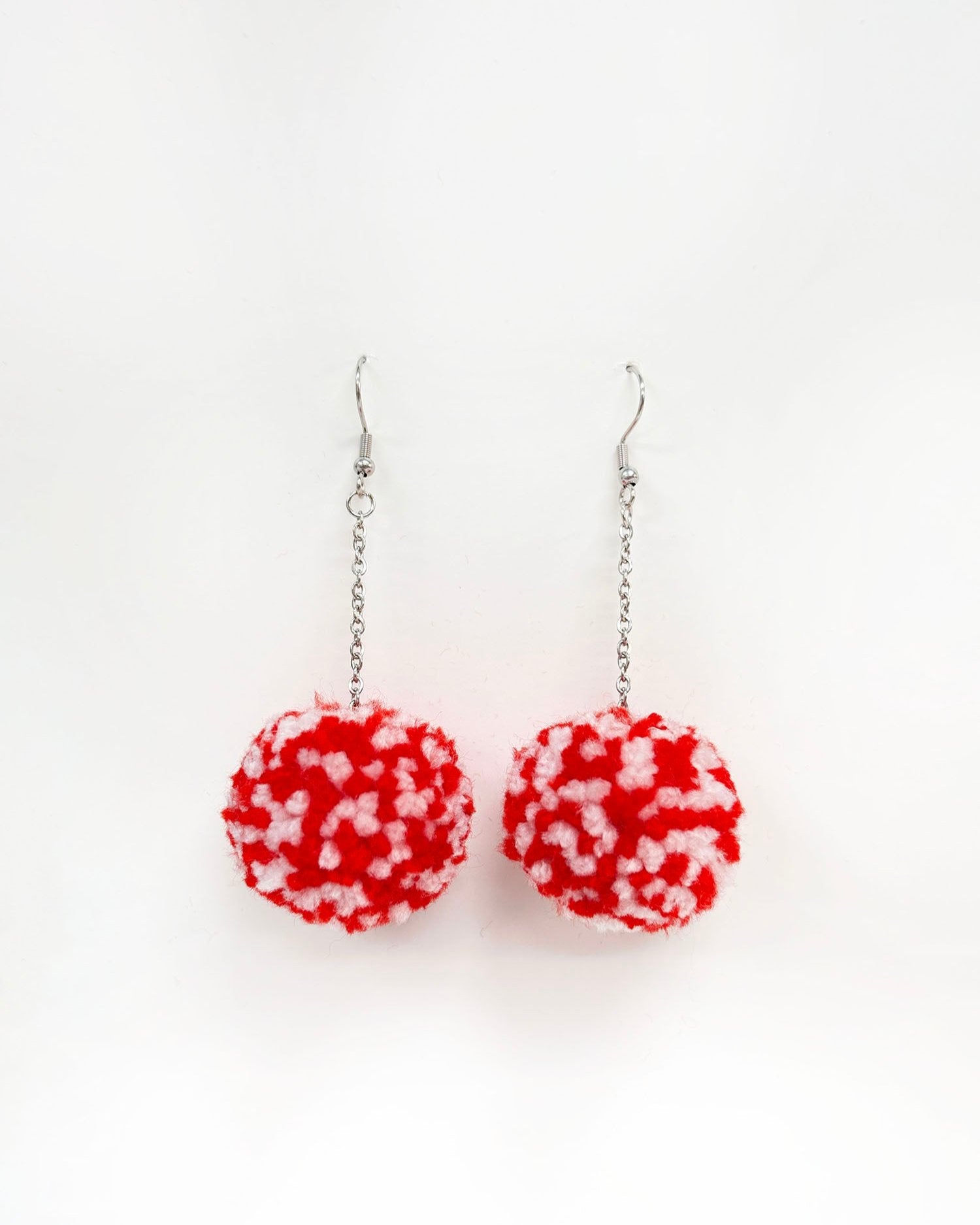 Pom pom rdeče beli božični uhani na beli podlagi.
