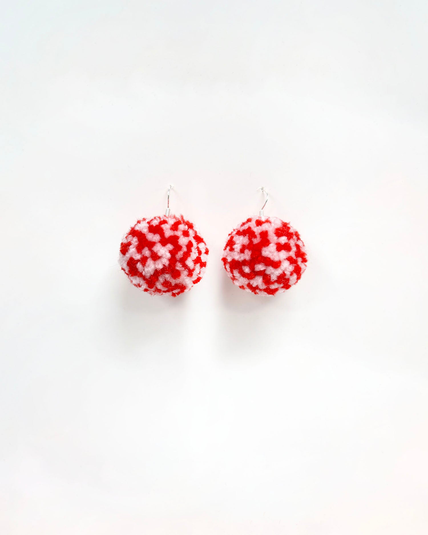 Pom pom rdeča bela uhani iz cofa na beli podlagi.
