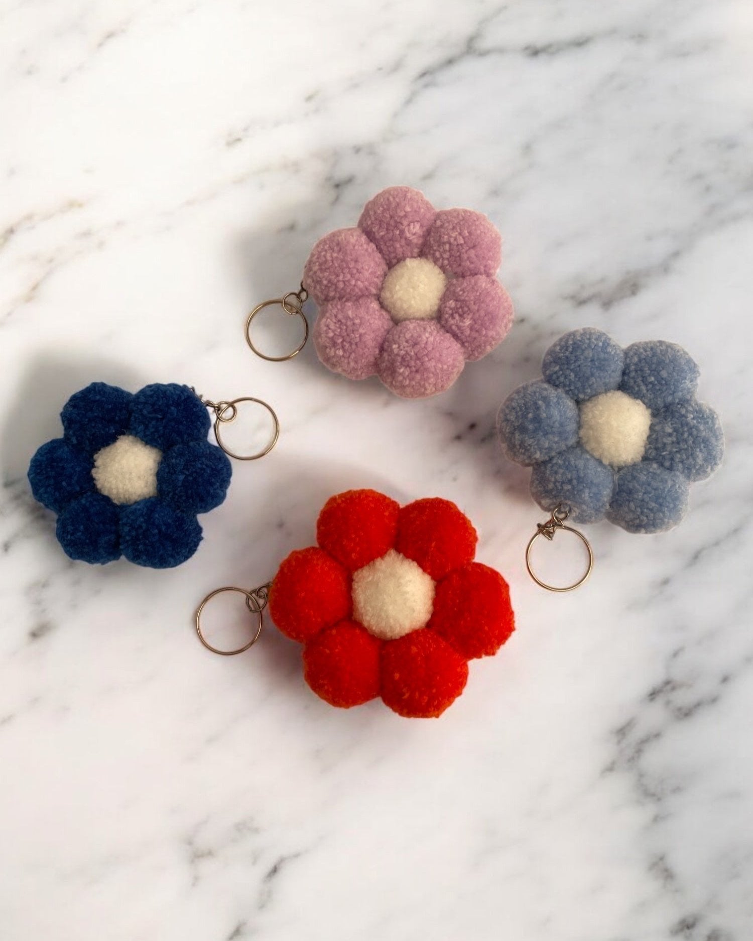 Pom pom obeski, v obliki rože, v različnih barvah, postavljene na marmor.
