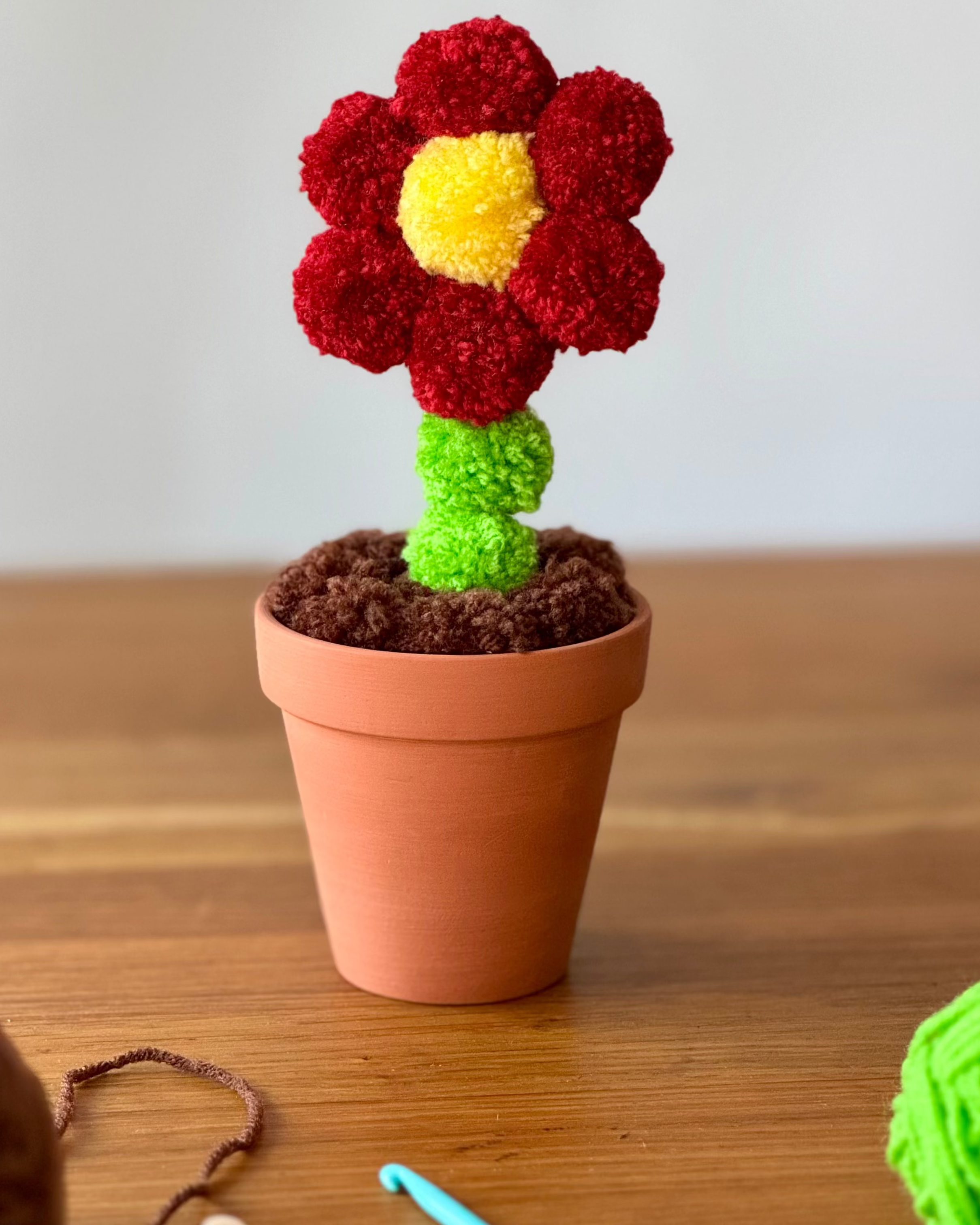 Pom pom roža iz cofov, v glinenem lončku, preja volne, lesena miza