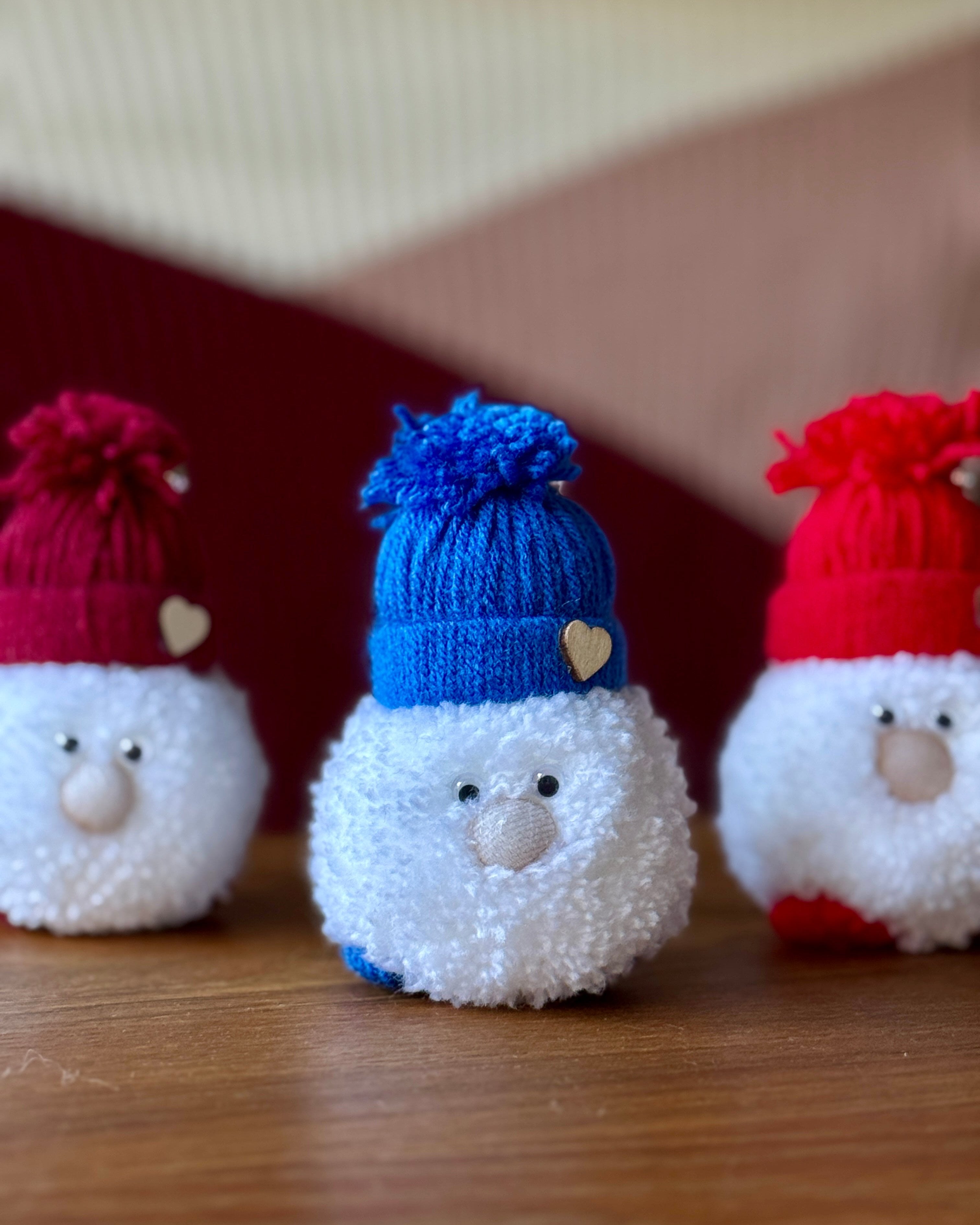 Prisrčen božični škrat, ročno izdelan iz mehkih pom pomov, lesena miza, božično vzdušje