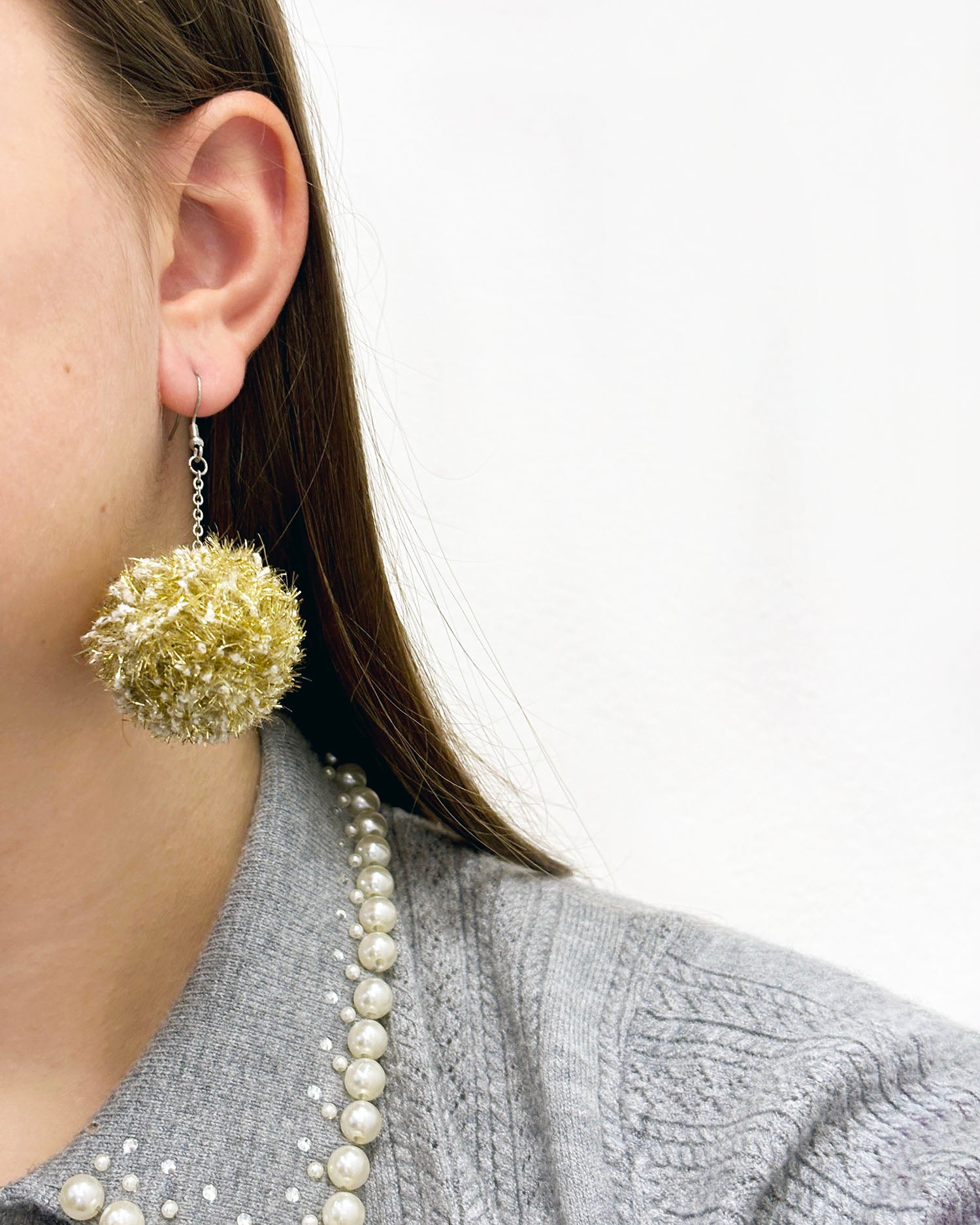 Pom pom uhani iz volne ter bleščečih trakov, iz cofa, v zlati barvi v ušesu.
