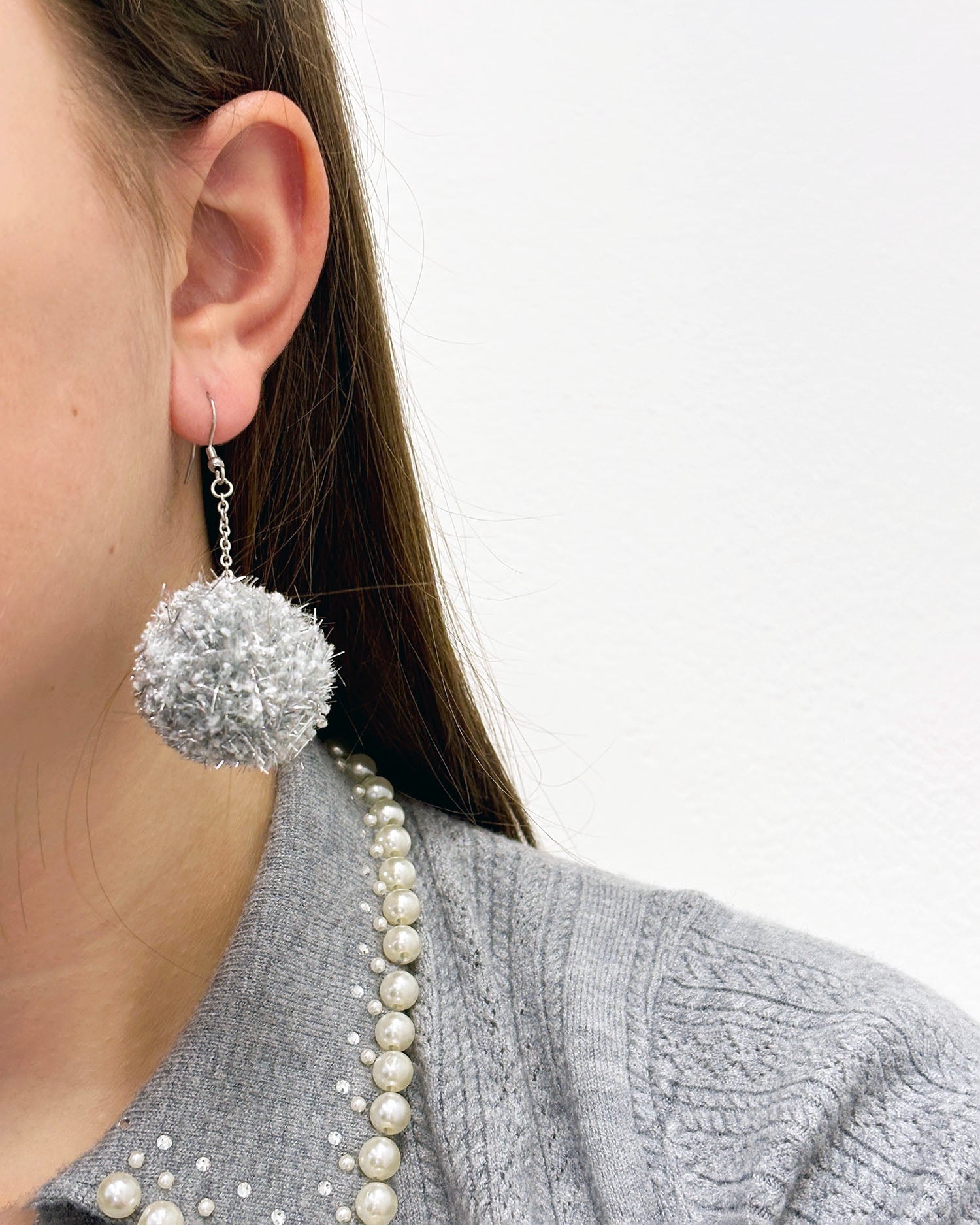 Pom pom uhani iz volne ter bleščečih trakov, iz cofa, v srebrni barvi na zlati podlagi.
