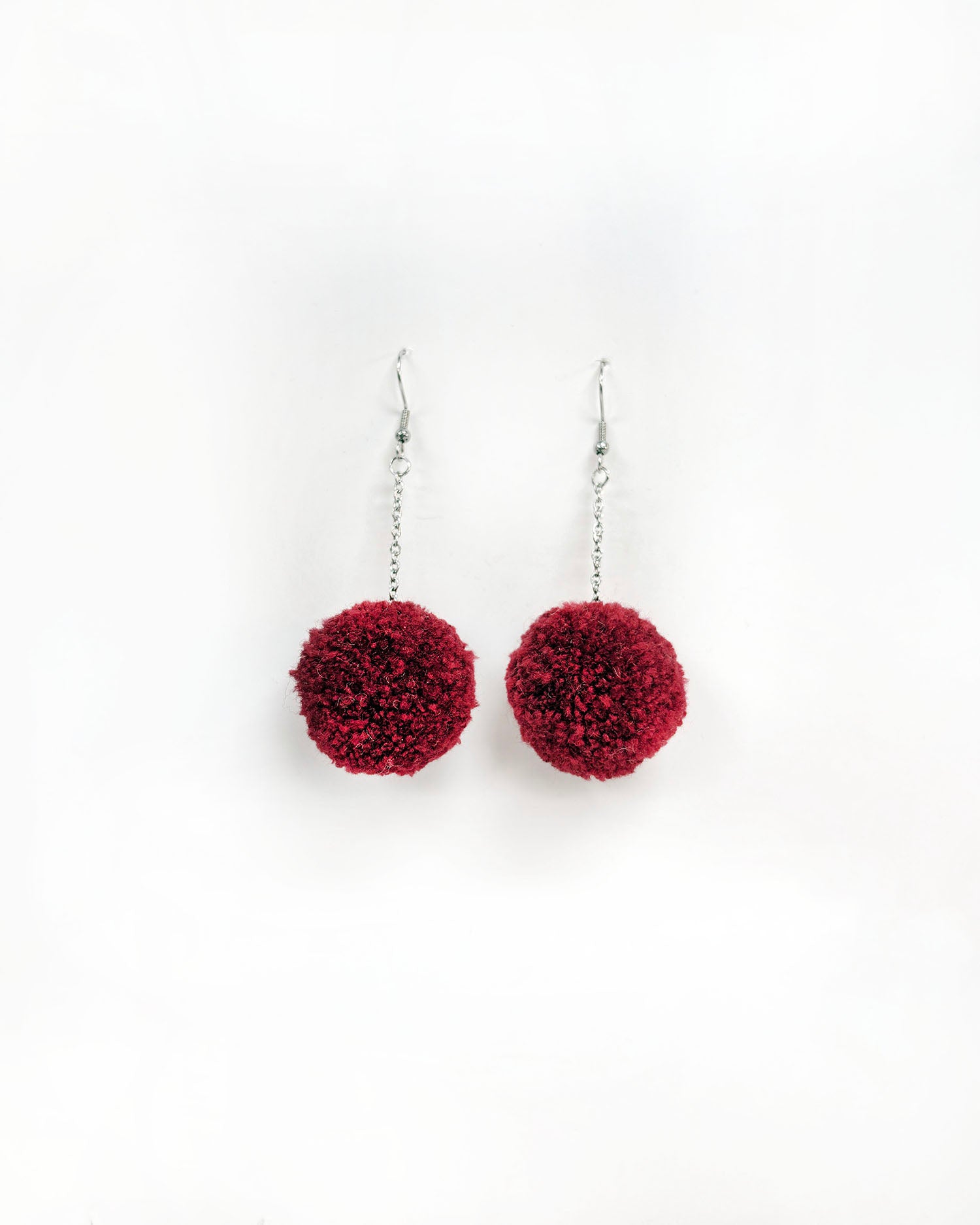 Pom pom uhani bordo rdeča barva, cof na beli podlagi.
