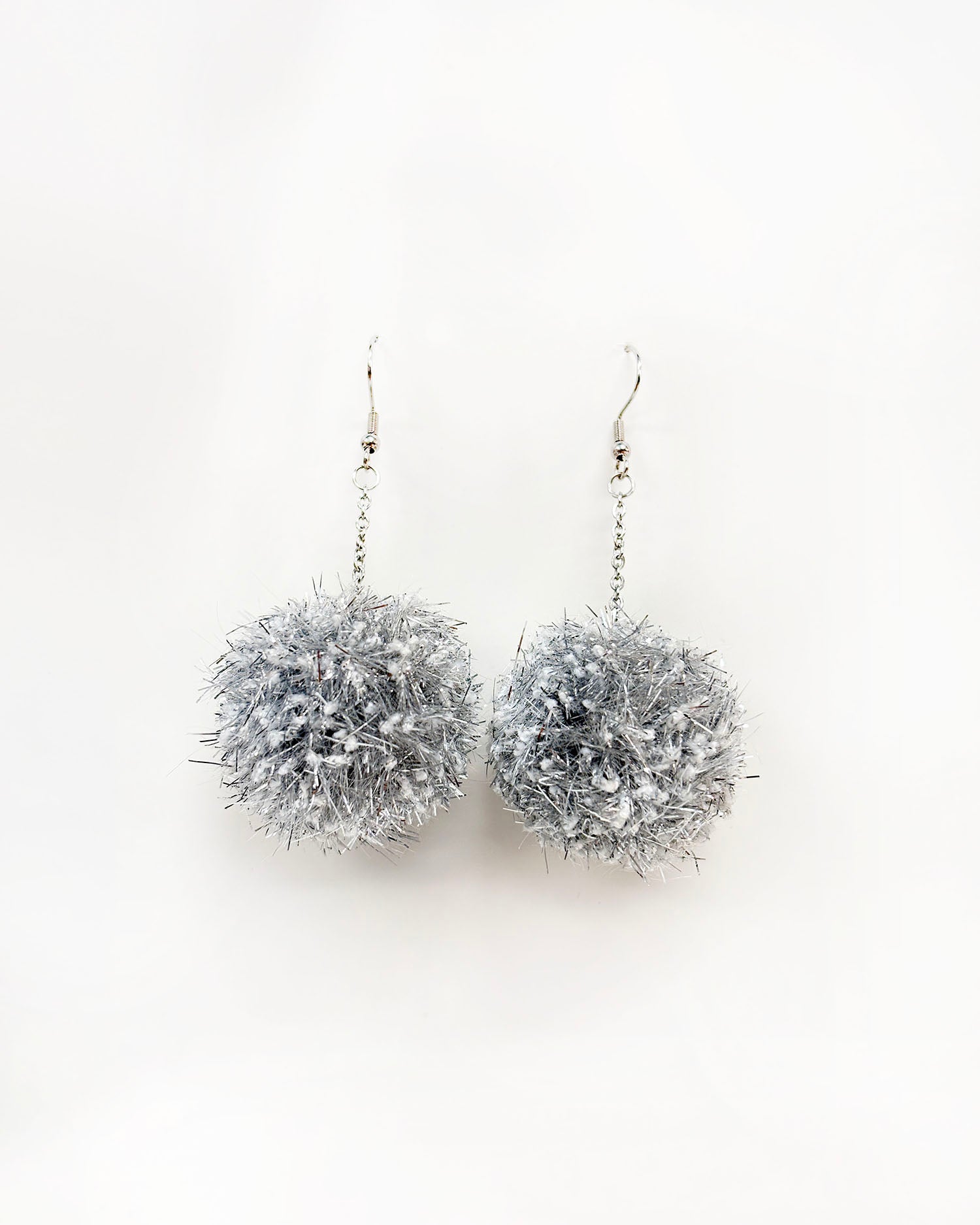 Pom pom uhani iz volne ter bleščečih trakov, iz cofa, v srebrni barvi na beli podlagi
