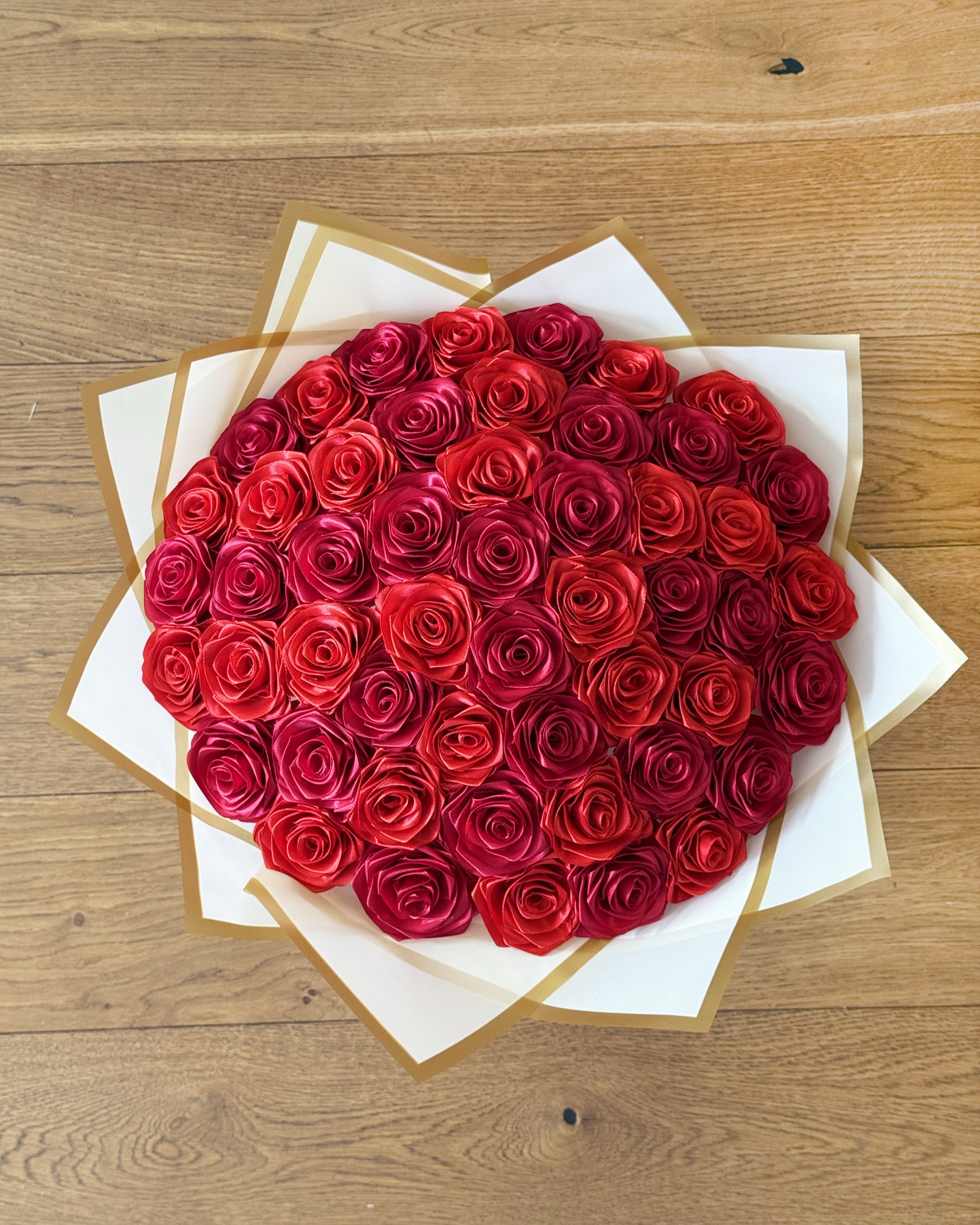 Satenast šopek vrtnic v rdeči in bordo rdeči barvi, zavit v bel korejski papir, slikan od zgoraj navzdol.