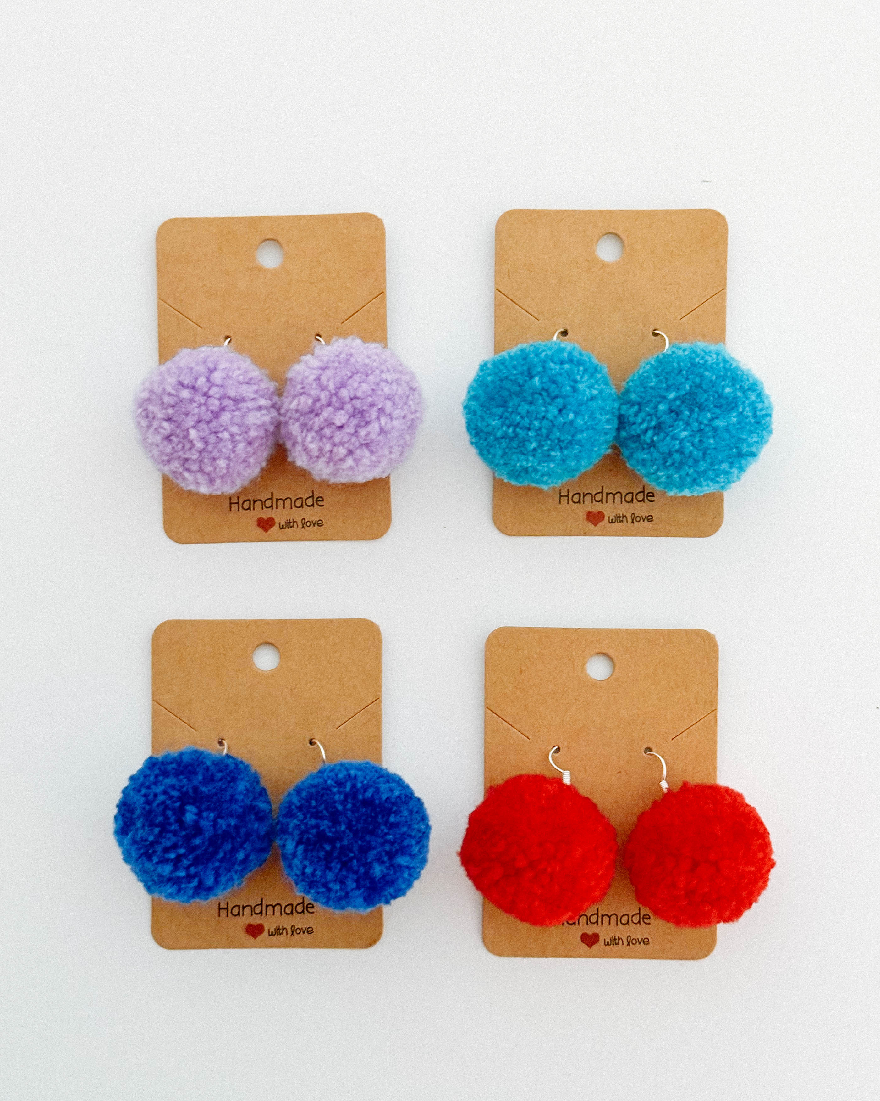 Štrije pari pom pom uhanov iz cofov v različnih barvah na mizi.
