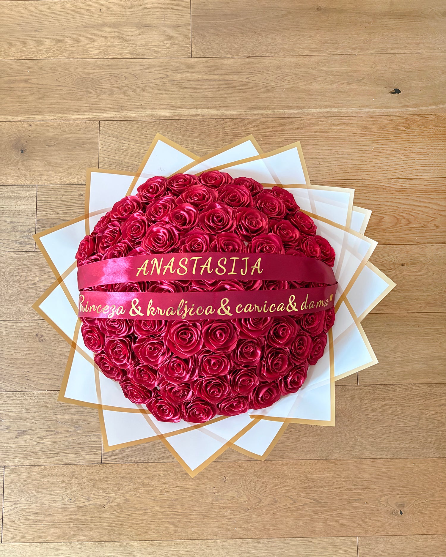 Bordo rdeč satenast šopek iz vrtnic, ovite z v bel korejski papir, z zlatim napisom. 