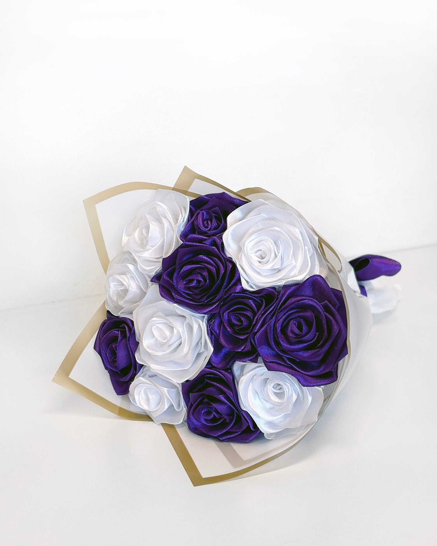 Šopek vrtnic iz satenastega traku v vijolično-beli barvi na polici.