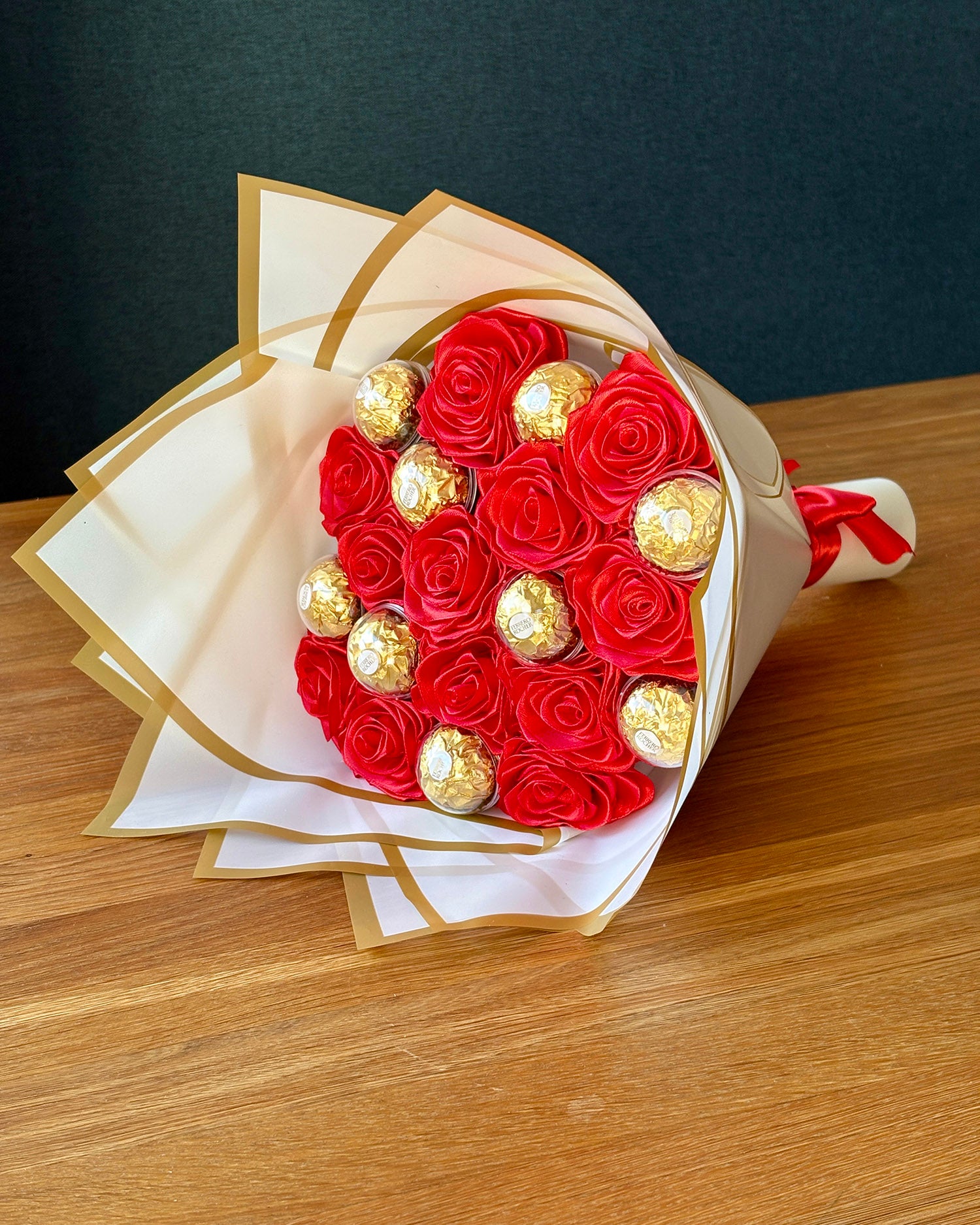 Rdeč šopek iz satenastih vrtnic, z ferrero roschejem na rjavi mizi
