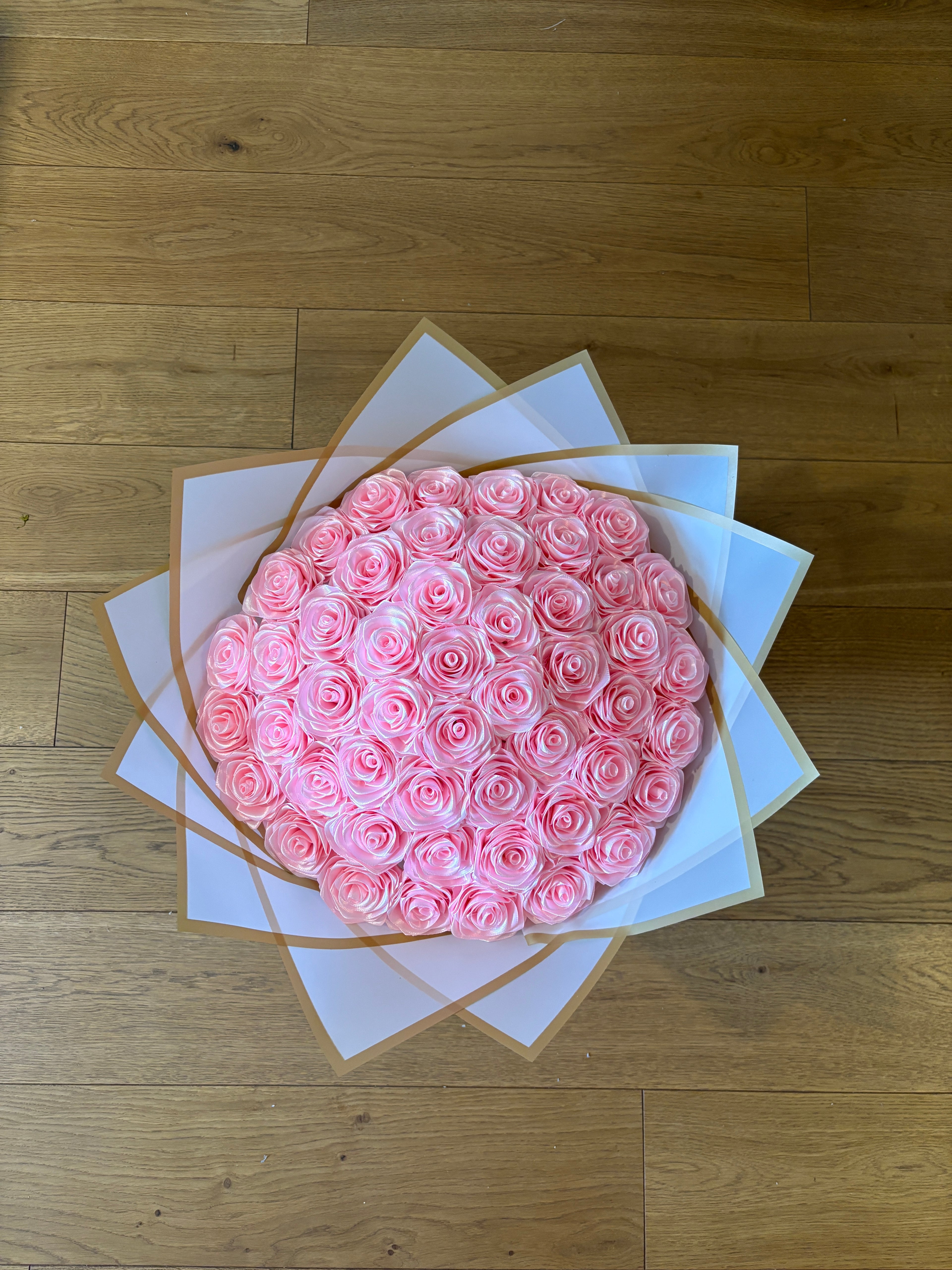 Satenast šopek vrtnic v roza barvi, zavit v bel korejski papir z zlatim robom, slikano od zgoraj navzdol
