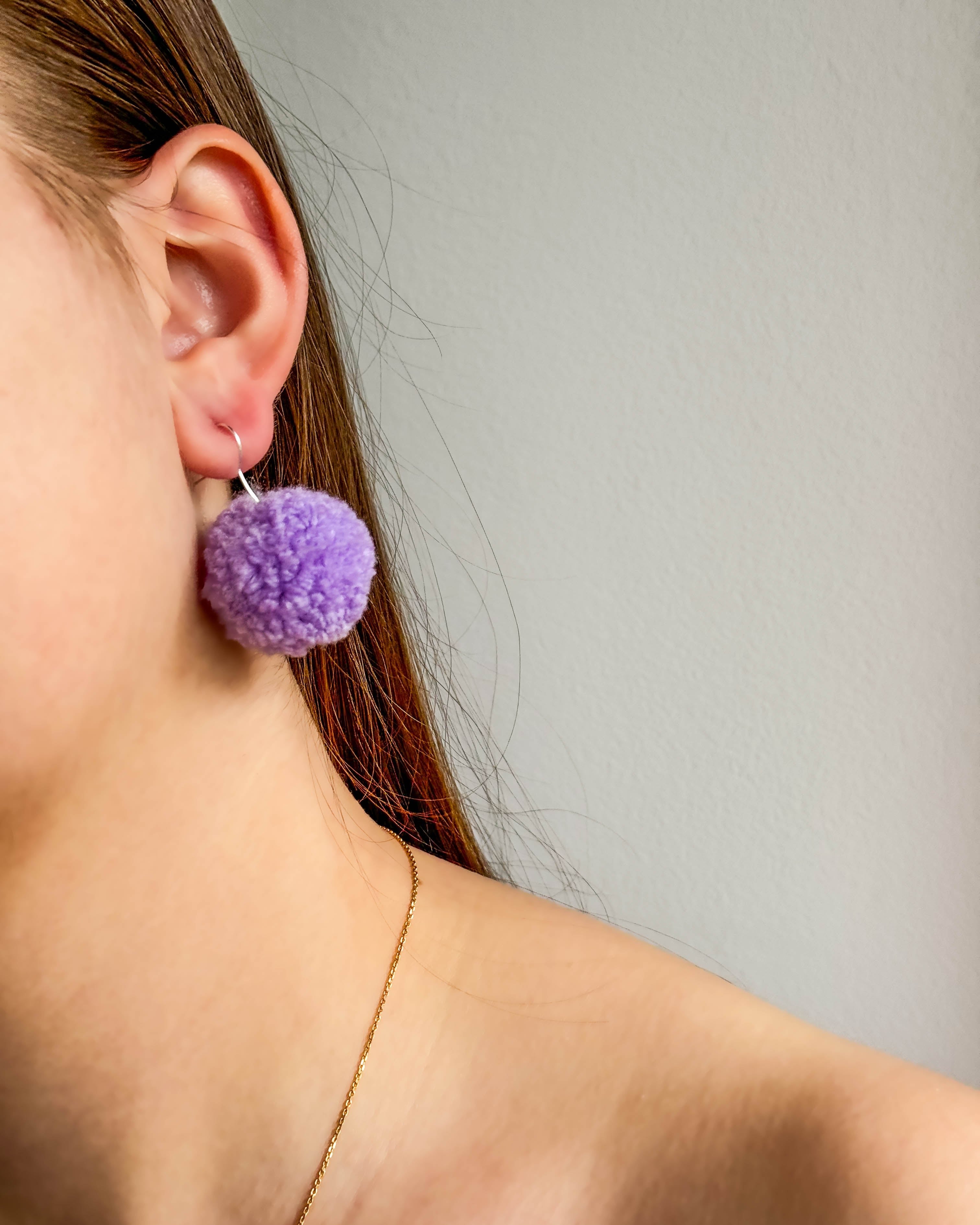 Pom pom vijolični uhani v ušesu ženske z dolgimi lasmi.