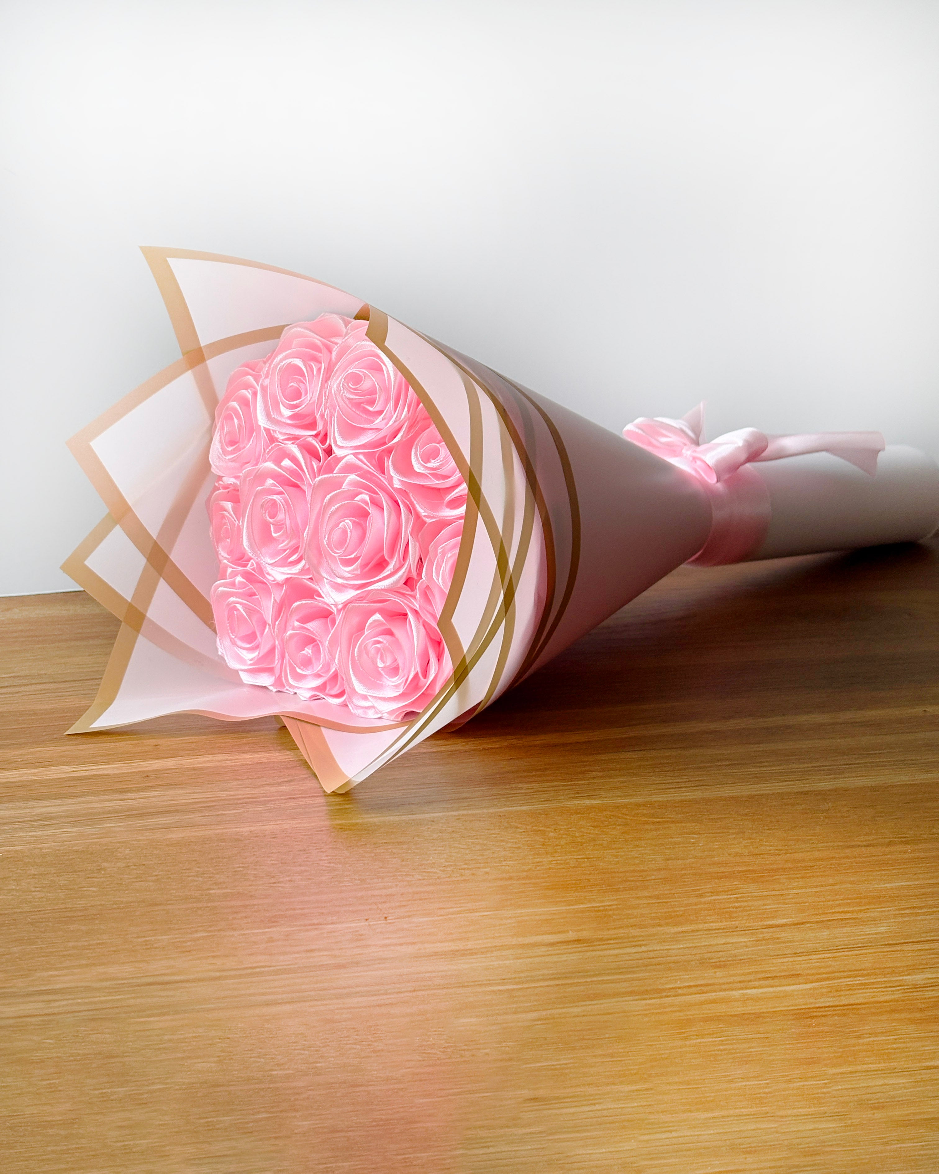 Šopek vrtnic, svetlo roza barve, zavit v bel korejski papir, postavljen na mizo
